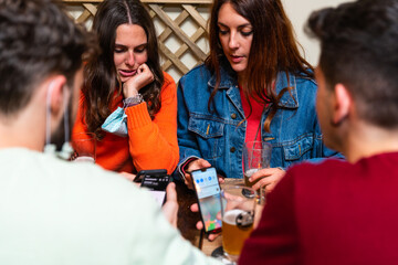 Caucasian young people using mobile smartphone at pub.