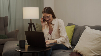Calm European woman works at home at the computer and talks on the phone.