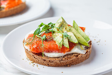 Breakfast toast with cream cheese, salmon and avocado, white background.