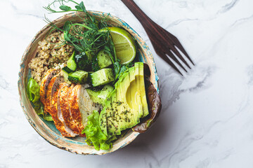 Quinoa salad with grilled chicken breast, avocado and cucumber in ceramic bowl on white marble background. Balanced diet concept.