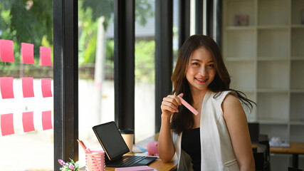 Happy young asian woman sitting in modern workplace and smiling to camera.