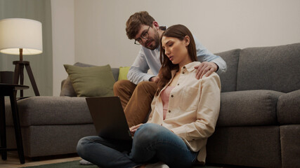 The man sits on the sofa next to the girl who is working and he massages her shoulders .