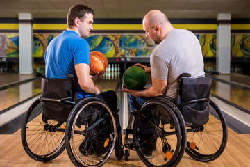 Two young disabled men in wheelchairs playing bowling in the club