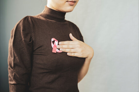 Woman touching her breast with pink badge ribbon on her brown sweater. Breast cancer awareness concept.