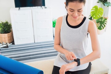 Asian woman resting and using smart watch after play yoga and exercise at home background with copy space.Concept of sport technology to checking health data.