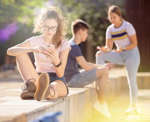 Teen girl sitting with phone separately on summer city street. Concept of lack of real...