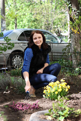 Brunette girl works in a spring garden, plants flowers and soil grab with special rakes