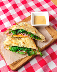 Ham and fresh vegetables in pita bread on wooden table with red plaid tablecloth.