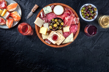 Fototapeta na wymiar Buffet with wine and appetizers on a black background. Italian delicatessen. A platter of snacks with salmon, prosciutto, jamon, olives, and cheese. Overhead photo of food and drinks