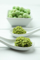 Tasty wasabi nuts and sauce on white wooden background