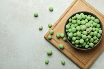 Board with bowl of wasabi nuts on white textured background