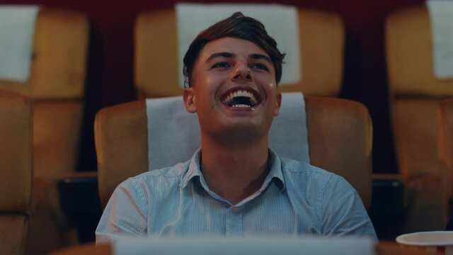 Attractive cheerful young caucasian man laughing while watching film in movie theater. Lifestyle entertainment concept. Close up shot.