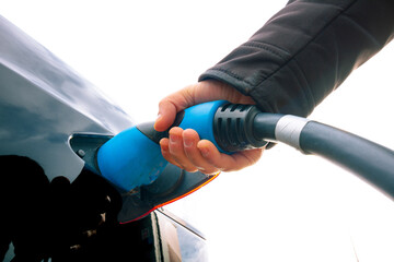 Man holding an attached charger on the Electric Vehicle in focus from below