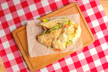 Ham and fresh vegetables in pita bread on wooden table with red plaid tablecloth.