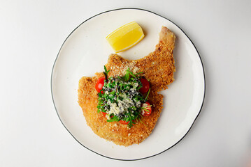 One deep fried fish bone steak with cherry tomatoes and fresh arugula on top.