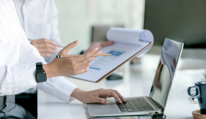 Cropped shot of business people hands holding pencil and using laptop computer while sitting at the table in office.