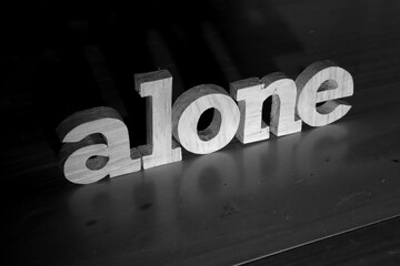 Alone, text words typography written with wooden letter on black background, life and business negativity