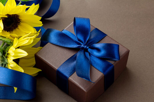 鮮やかな青いリボンで結んだ茶色の箱とひまわりの花とこげ茶色の背景のプレゼントのイメージ