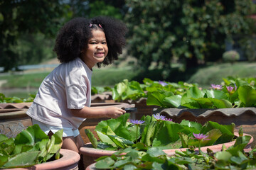 Naklejka na ściany i meble Childhood and environment conservation concept - little African American curly hair girl using magnifying glass looking pollen lotus flowers.