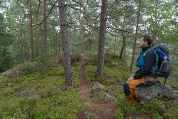 Fototapeta na wymiar Man sitting with backpack looking at horizon in forest. Relaxing.