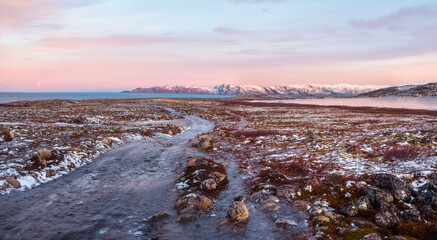 Icy winter road through the tundra hills in Teriberka. Wonderful panoramic mountain landscape with tundra on the Barents sea.