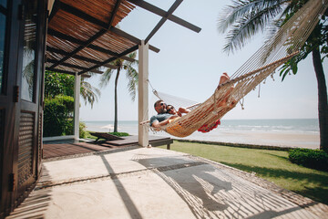 Couple relaxing in a hammock by the beach - Powered by Adobe