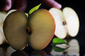 Composition with apple slices on a black background. A slice of apple with back light on a black background with water drops. Juicy apple on a table.