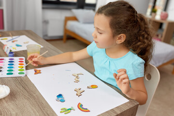 childhood, hobby and leisure concept - little girl with brush painting wooden chipboard items at home
