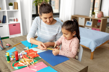 family, art and craft concept - mother spending time with her little daughter with glue making applique of color paper at home