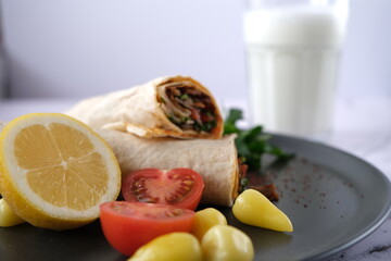Wrap, tomatoes, pickled peppers, parsley and buttermilk in a glass cup on a black porcelain plate