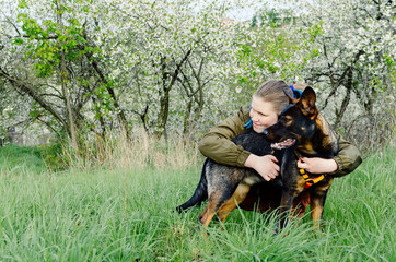 A teenage girl with blue hair is hugging her Australian kelpie dog and looking away. 