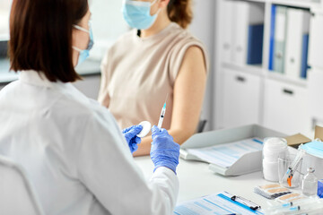 Fototapeta premium health, medicine and pandemic concept - female doctor or nurse wearing protective medical mask and gloves with syringe vaccinating patient at hospital