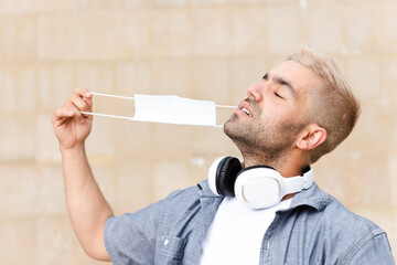 End of Coronavirus pandemic and feeling free concept. Hispanic young man with blond hair removing the face mask and breathing.