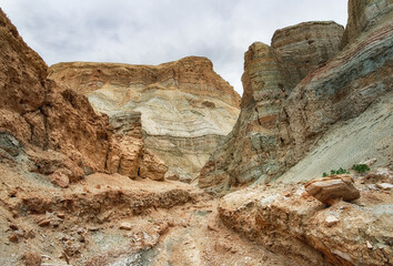 Fototapeta premium A canyon among the ancient desert steppe fields, geological deposits of different times, clay, erosion, stones. Rocky cliffs, hills and mountains in the Altyn-Emel park in Kazakhstan. Sky with clouds.