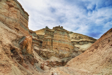 A canyon among the ancient desert steppe fields, geological deposits of different times, clay, erosion, stones. Rocky cliffs, hills and mountains in the Altyn-Emel park in Kazakhstan. Sky with clouds.