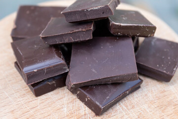 Pieces of dark chocolate lie on a wooden cutting board.