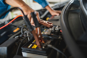 Auto mechanic is charging the battery. He works in a garage. Car repair service and car problems concept.