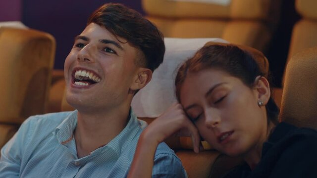 Attractive cheerful young caucasian couple laughing while watching film in movie theater. Lifestyle entertainment concept.