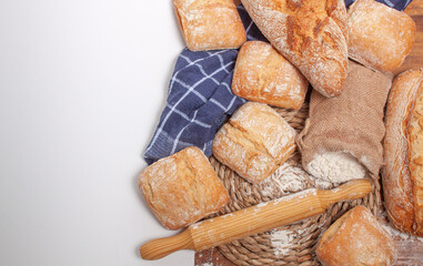
Vista de un montón de pan colocado a la derecha con un salvamanteles de esparto, un rodillo de madera para hacer el pan y un pequeño saco de harina con un espacio en blanco para el texto . - obrazy, fototapety, plakaty