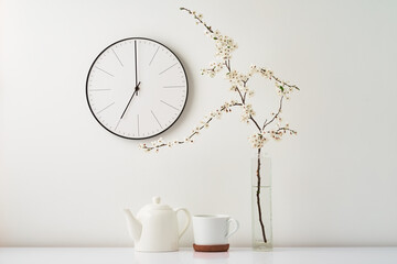 Wall clock, blooming branch and cup on white background