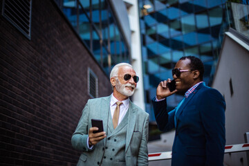   Two business men talking on the street. Using smart phones.