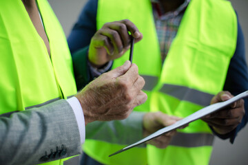 Mature engineer discussing the structure of the building with architects colleague at construction site. Signing document.