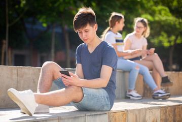 Teen guy plays on smartphone on city street