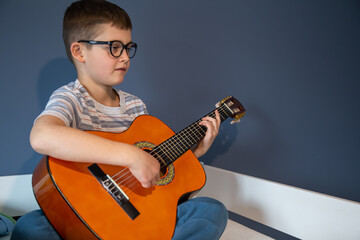 Little boy plays the classical guitar at home, on the bed.
