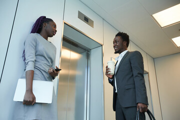 Low angle view at two African-American business people waiting for elevator in office building and...