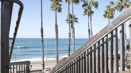 Wooden stairs, beach access in Oceanside, California USA. Coastal stairway, pacific ocean waves and palm trees. Vacations by sea in United States. Sunny tropical day, summertime aesthetic. Staircase.