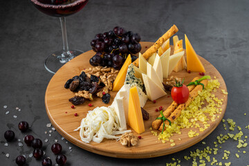 Cheese plate served with grapes, jam, figs, crackers and walnuts on a dark stone background