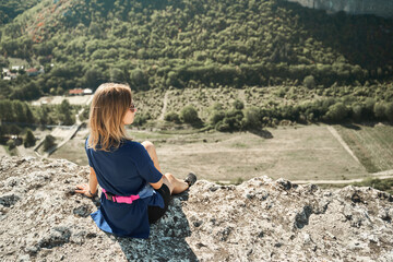 Naklejka premium Young woman sits on a rock, looking at the landscape and enjoying the view and fresh air.