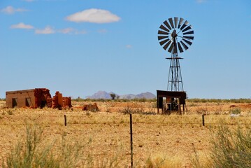 Windmill water pump in the Namibian desert with an abandoned building next to it, on a sunny day with blue sky and some clouds