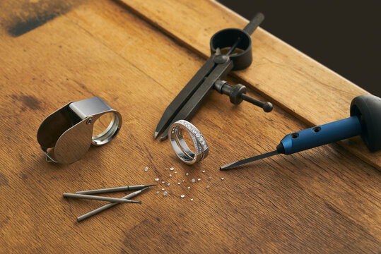 Workplace of a jeweler. Tools and equipment for jewelry work on an antique wooden desktop. Jeweller, engraver at work on jewelry made of diamonds and gold. Wood Platinum Diamond Metal Background